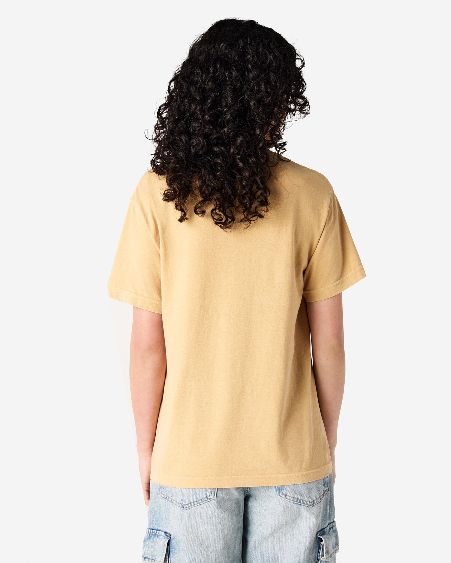 Back view of woman wearing faded mustard American Apparel Heavyweight Unisex T-Shirt with long curly hair looking to the right