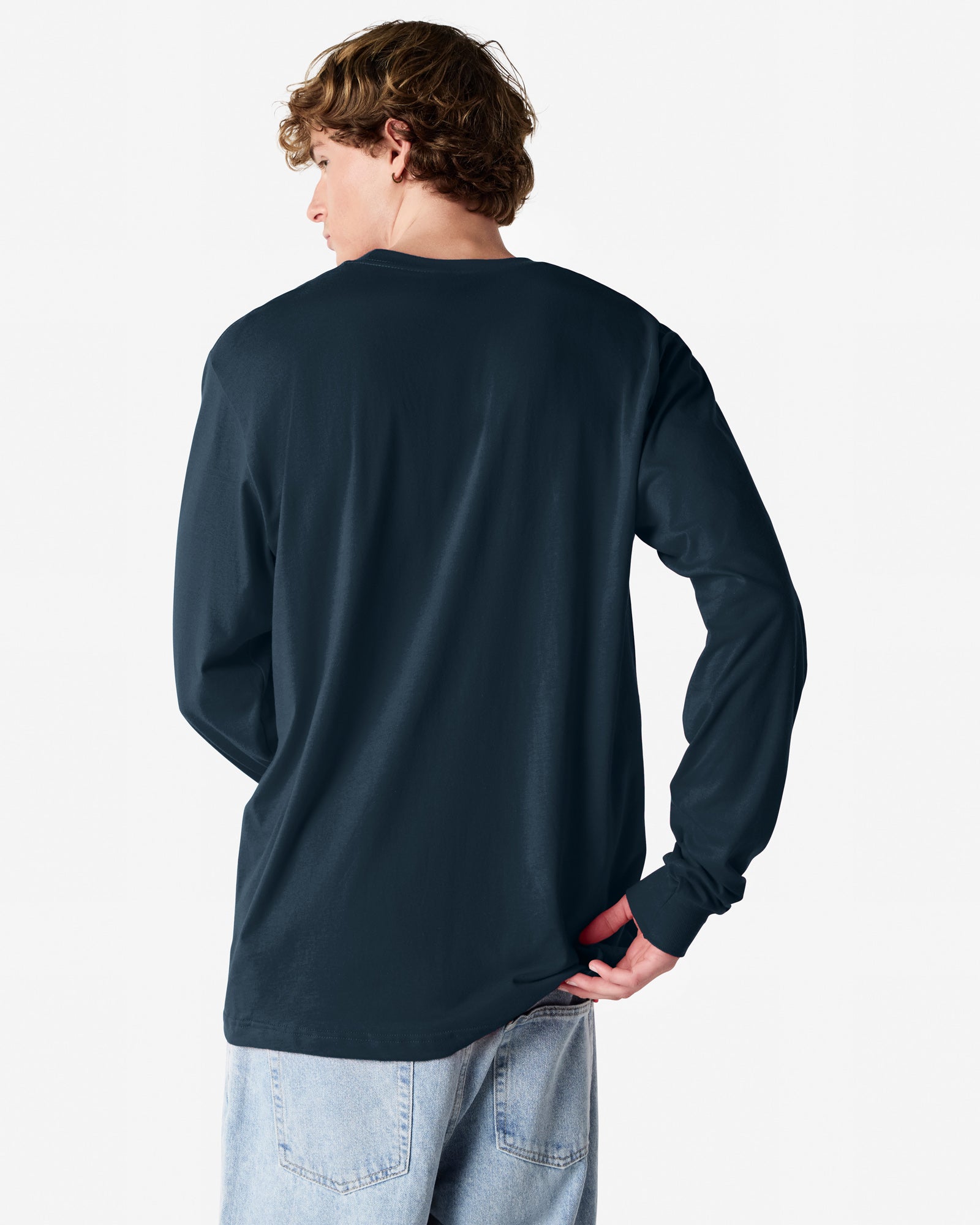 Back view of man wearing navy American Apparel Fine Jersey Long Sleeve Unisex T-shirt with right hand near back pocket looking left
